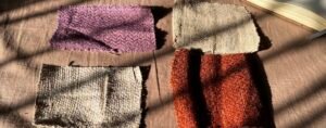 Four woven textile swatches in purple, natural, gray, and rust tones arranged beside a notebook during a search for hemp in Kathmandu.