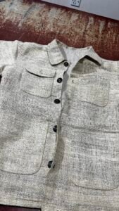 Handwoven hemp chore jacket first sample laid flat on a workbench in a Kathmandu workshop