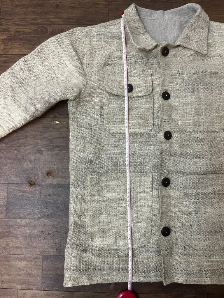 Handwoven hemp chore jacket sample laid flat and buttoned, with a tape measure in frame