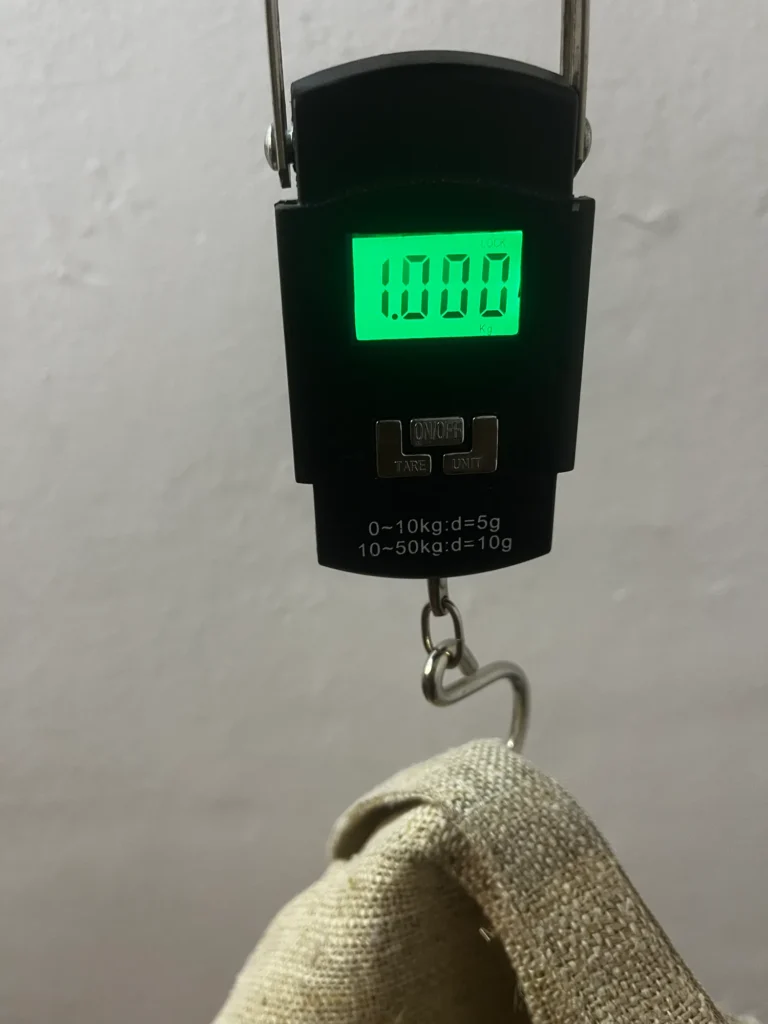 Hanging scale reading 1.000 kg, with a handwoven hemp chore jacket sample hooked underneath