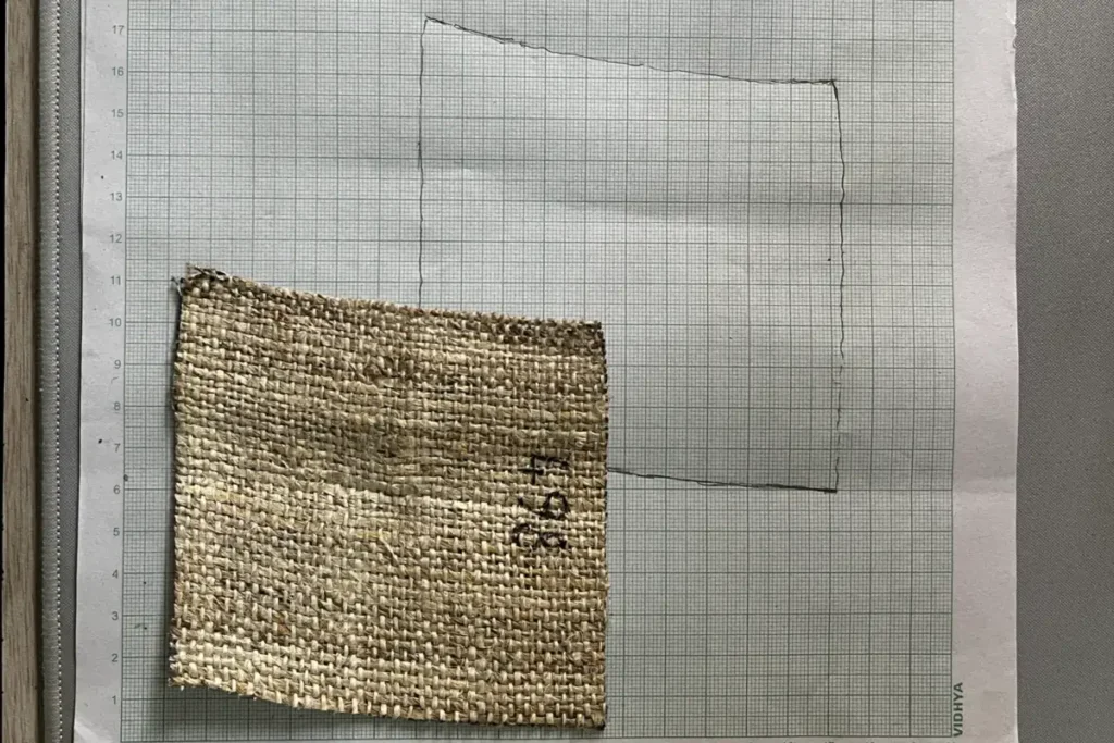 A trimmed handwoven hemp swatch on graph paper beside the outline traced from it, which is slightly out of square
